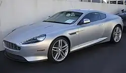 A front three-quarters view of a silver 2013 facelift DB9 in a dark environment.