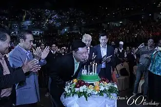 Chareonwongsak blowing out birthday candles, surrounded by people