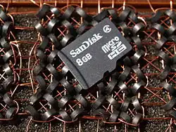 This microSDHC card holds 8 billion bytes (8 GB). It rests on a section of magnetic-core memory that uses 64 cores to hold eight bytes. The microSDHC card holds over one billion times more bytes in much less physical space.