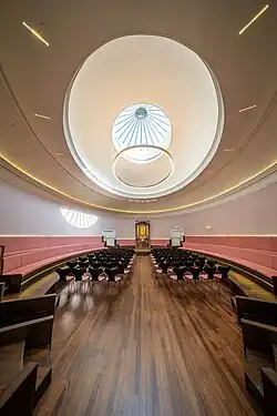 The Sypert Concert Room at St Cecilia's Hall with rows of chairs and pink benches lining the walls, the room is an elliptical shape and has an elliptical glass dome on the ceiling