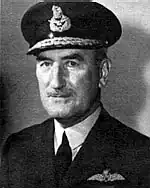 Head-and-shoulders portrait of man in dark uniform with peaked cap and pilot's wings on left-breast pocket