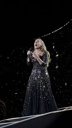 Adele sings into a microphone wearing a black dress