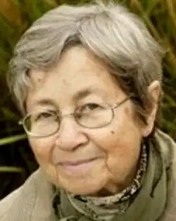 Colour publicity shot of a smiling, bespectacled woman with short, grey hair.