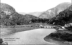 View of a river crossed by a wooden bridge, with brushy hills in the distance