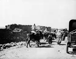 People on foot and on donkeys walk past mud huts.