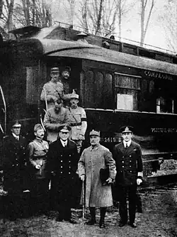 black and white photograph of five men in military uniforms standing side-to-m right, seen outside his railway carriage No. 2419&nbsp;D in the Forest of Compiègne.