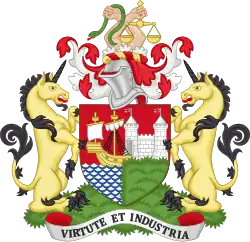 Acoat of arms, with a shield showing a sailing ship and a castle with maned lions on either side, surmounted by the helmet from a suit of arms and two hands holding a snake and scales of justice. The motto at the bottom is "Virtute et Industria"