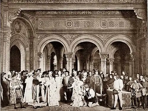 photograph of stage, large cast in 16th century costumes, indoor scene, with young couple bowing to the King of France