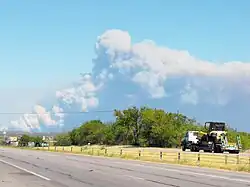 Photograph of a large brown/gray smoke plume emanating from the horizon on a clear afternoon