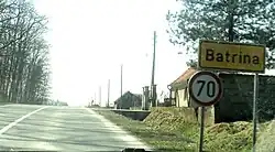 A road with a grassy verge and some houses on the right hand side. A 70kmph sign is in the right hand corner.