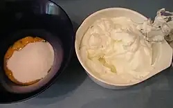 Two bowls. One contains egg yolks with white sugar. The other contains whipped egg whites.