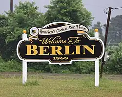 A black, white, and yellow sign that reads "America's Coolest Small Town: Welcome to Berlin 1868"