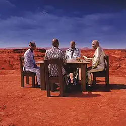 Four men sitting by a table at Bardenas Reales with horses on the table and the Earth and Moon in the background.