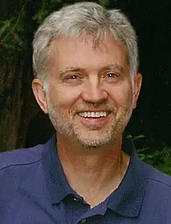 Portrait photo of a white man with short dark gray hair and a full beard wearing a blue polo shirt.