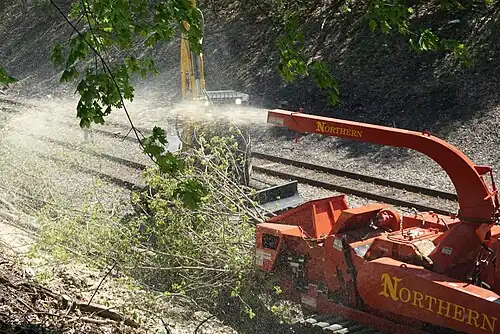 Brush being fed into a wood chipper next to a railway line