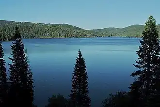 A large lake under blue skies surrounded by forested hills with steep slopes under a clear blue sky