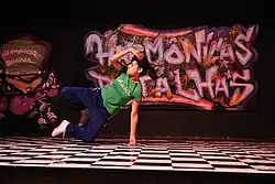 A woman who has black hair tied back and a green T-shirt is swinging herself sideways onto one arm, both feet off the ground.