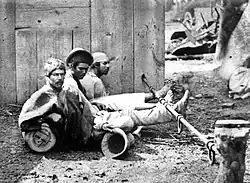 Trio of men seated on the ground with ankles shackled to a pole lying horizontally