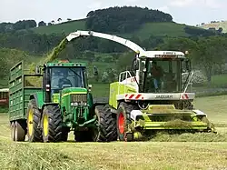 A tractor with a trailer running beside a self-propelled Claas Jaguar forager