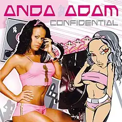 Anda Adam is shown wearing pink shorts and a crop top. Next to her, a cartoonified version of Anda having a similar pose can be seen. CDs and Vinyls can be spotted in the white and pink background.
