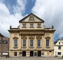 An imposing eighteenth-century building with three entrance archways, large first-floor windows and an ornate peaked gable end above.