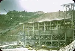 Large metal building in front of a mountain with large portions cut out