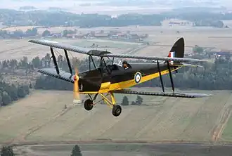 Colour photograph of a black and white biplane flying above a rural area.