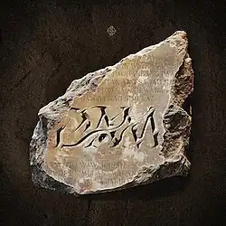 The cover art for "Dam": A chipped stone tablet with the song's title, "Dam", and song lyrics engraved, placed on a dark brown background. SB19's logo is placed above it.