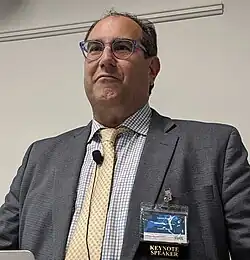 Middle aged Native American man wearing a suit and standing at a podium