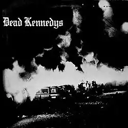 A black-and-white photograph of a burning car outdoors at night. In the upper-left corner are the words "Dead Kennedys" in Gothic script.