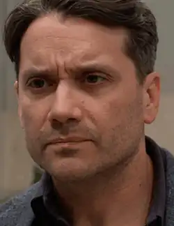 A dark-haired male with facial hair in a dark t-shirt.