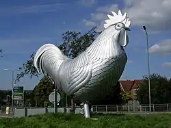 A large, shiny, metallic sculpture of a chicken facing right