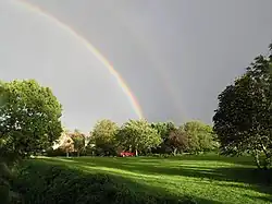 double rainbow over green in bright sunshine with large tree on both left and right of image