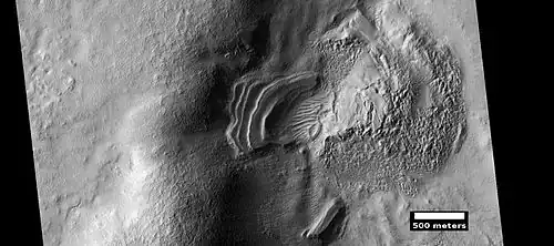 Layered feature that is probably the remains of a once widespread unit that fell from the sky, as seen by HiRISE under the HiWish program. Dipping layers are common in some regions of Mars. They may be the remains of mantle layers. Another idea for their origin was presented at 55th LPSC (2024) by an international team of researchers. They suggest that the layers are from past ice sheets.[61]