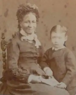 Photograph of a dark-skinned woman in a Victorian-era dress seated next to a standing child