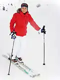 A female skier in winter clothes: jacket, hat, thick gloves, warm pants and ski boots
