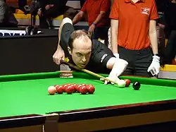 Fergal O'Brien leans across a snooker table holding his cue lining up a shot to a corner pocket