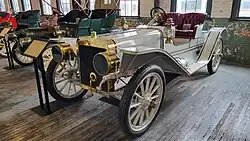 A white-colored, old-fashioned car with four seats and brass fittings