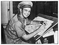 A photo of Fred Lasswell posing while inking a cartoon at the drawing board. Fred is in a Marine Corps uniform.
