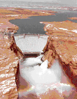 Glen Canyon Dam releasing floodwater. A rainbow is visible over the Colorado River.