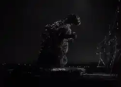 Dark night scene with city lights in the background, with a massive dinosaur-like creature stands on hind legs facing tall electrical towers