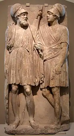 Stone slab with two men carved on it. They stand, wearing chitons.