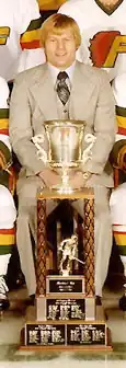 Middle-aged man dressed in a grey suit sitting behind a large trophy in a hockey team photo