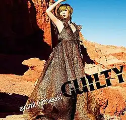 Ayumi Hamasaki show from top to bottom, looking outward, wearing a long leopard print dress, and with her right hand over her head. Behind her is what looks to be a view of the Grand Canyon. On the bottom is written slanted slightly in small lowercase white text "ayumi hamasaki" and next to it in large uppercase black text "Guilty."