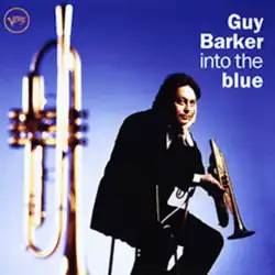 A photo of Barker sitting with one hand on his face and the other holding a trumpet, with another trumpet partially seen out-of-focus in the foreground.