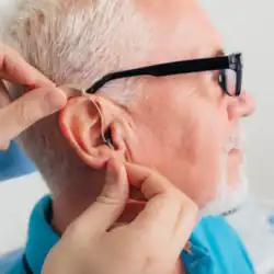 A technician places a new hearing aid in an older man's ear