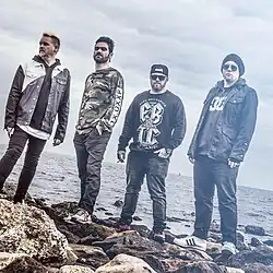 Four men standing on a rocky beach shore.