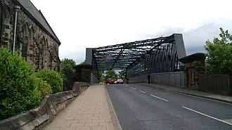 A slightly humped road bridge with iron struts along the sides and cross-hatched over the top
