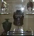 Hoplite armour exhibit. Note the gold inserts around the chest area of the bronze upper torso plate at the centre of the exhibit. The helmet on the upper left is a restored version of the oxidised helmet on the right.