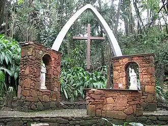 A stone altar with two images of Christian saints in a garden and on it a bow bearing a cross